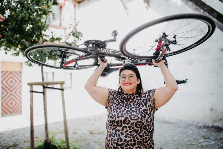 Sabine im Leopardenkleid hält ein Rennrad über dem Kopf hoch und lacht